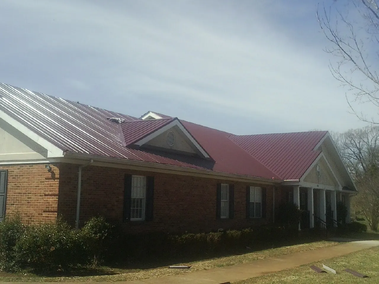 Red metal roof with gabled entries on a long brick building, from a Hail Damage Roof Repair job in Santa Rosa